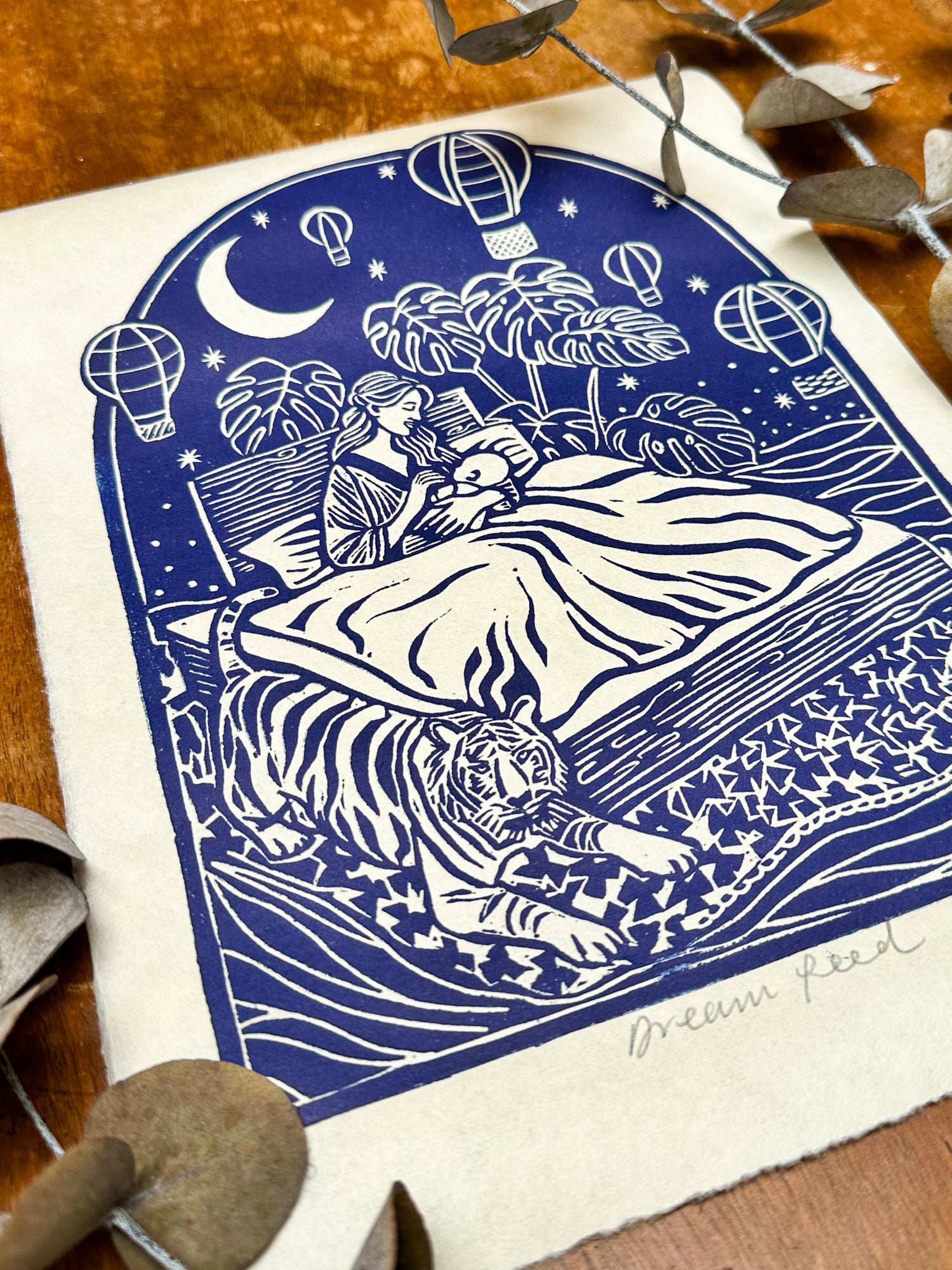 Decorative print of a woman feeding a baby in bed, which is floating on the sea. They are surrounded by a tiger, a monstera plant, the night sky and hot air balloons.